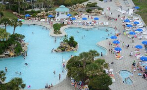 Una gran piscina al aire libre con varias secciones, rodeada de sillones de descanso y sombrillas.
