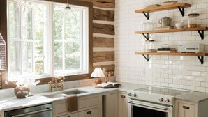 A kitchen with white cabinets, a stainless steel dishwasher, a built-in oven, and a window with natural light. - Modern Cabin By Bear Lake (Cookeville)