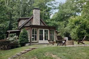 A rustic cabin with a stone chimney, large windows, and a wooden deck with Adirondack chairs. - Modern Cabin By Bear Lake (Cookeville)