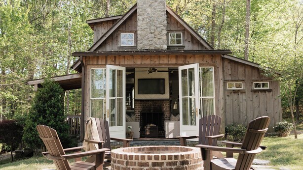A rustic cabin with a stone chimney, wooden exterior, and a fire pit surrounded by Adirondack chairs. - Modern Cabin By Bear Lake (Cookeville)