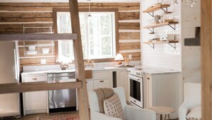 A rustic kitchen with wooden beams, white cabinetry, a chandelier, and a cozy seating area with a patterned rug. - Modern Cabin By Bear Lake (Cookeville)