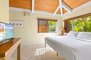 Une chambre à coucher avec un grand lit, un téléviseur posé sur un meuble en bois et une fenêtre équipée de stores.