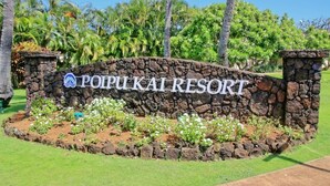 A sign for Poipu Kai Resort surrounded by a stone wall and lush greenery. - Hale Kai Kea | 3 King Suites, Bonus Room, Lanai & Tropical Paradise (Koloa)