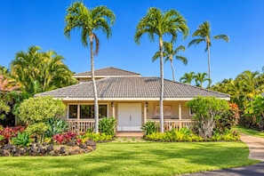A two-story house with a tiled roof, surrounded by a well-maintained lawn and tropical plants.