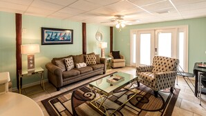 A living room with a brown sofa, patterned armchair, glass coffee table, and a framed painting on the wall. - Discounts Summer Very Short Walk to Beach - 2BD/2BA Sleeps 6 (Miramar Beach)