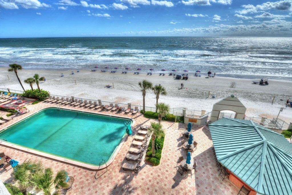 A beach view with a swimming pool, lounge chairs, and umbrellas.