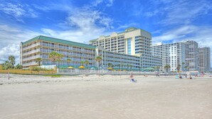 Un hôtel en bord de mer, avec plusieurs étages, des balcons et une plage en premier plan.