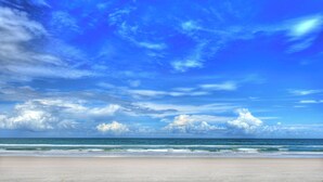 Une plage dotée d’un large rivage sablonneux et offrant une vue dégagée sur l’océan, sous un ciel bleu parsemé de quelques nuages.
