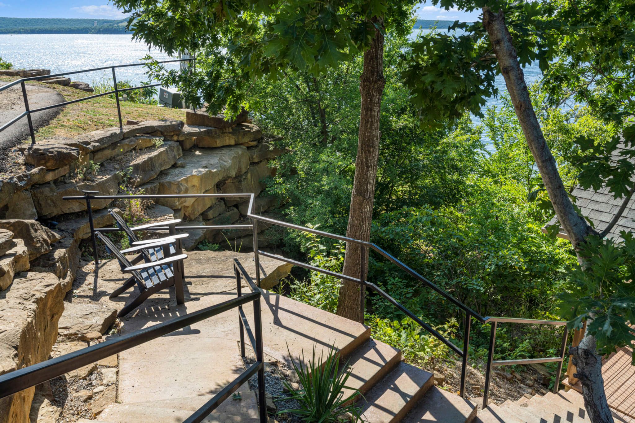 A stone staircase leading to a viewing platform with a metal railing, surrounded by greenery and overlooking a body of water.