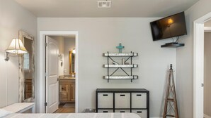 A bedroom with a bed, a TV mounted on the wall, a wooden ladder, and a shelf with a cross decoration. - Hideaway at CrossTimbers Marina (Sperry)