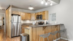 A modern kitchen with wooden cabinets, stainless steel appliances, and a bar area with metal stools. - Hideaway at CrossTimbers Marina (Sperry)