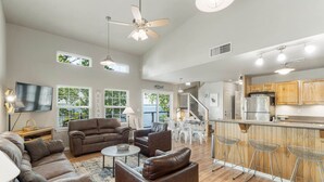 A spacious living area with a large sofa set, a coffee table, and a dining area with bar stools. There is a kitchen with modern appliances and wooden cabinets. - Hideaway at CrossTimbers Marina (Sperry)