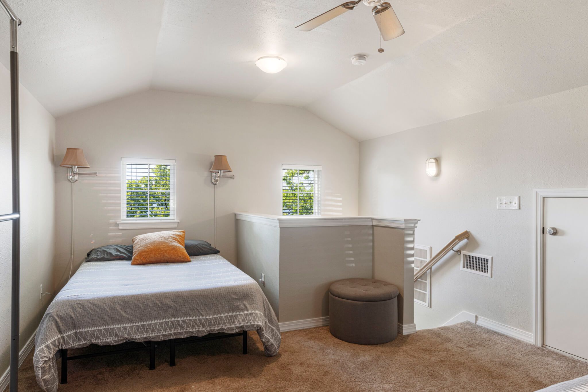 A bedroom with a bed, two windows, a ceiling fan, a radiator, and a door.