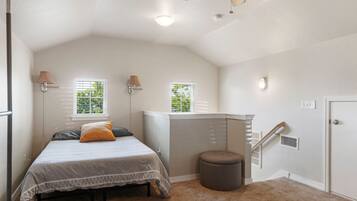 A bedroom with a bed, two windows, a ceiling fan, a radiator, and a door.