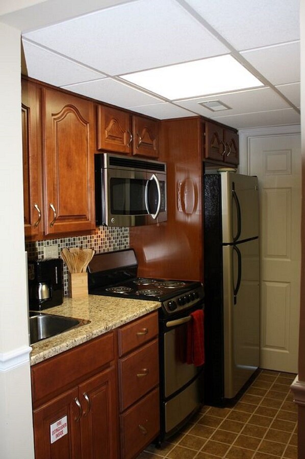 Una cocina con armarios de madera, un refrigerador de acero inoxidable, un microondas, una estufa y un salpicadero de azulejos.