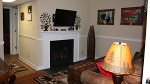 A living room with a fireplace, a television mounted above it, and a lamp on a table.