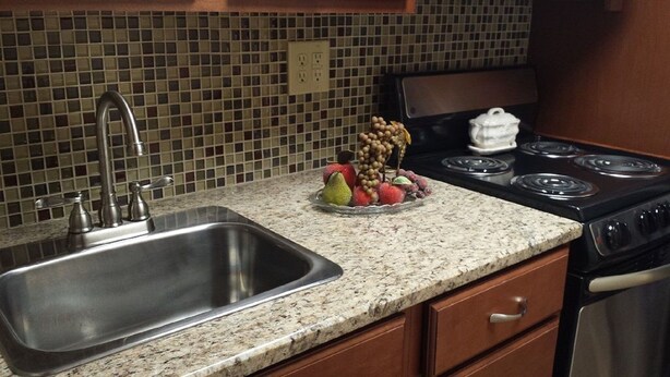 A kitchen with a granite countertop, stainless steel sink, and a stove with four burners.