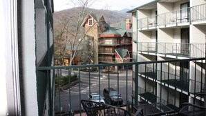A view from a balcony overlooking a parking area and a building with multiple balconies and a mountain backdrop.