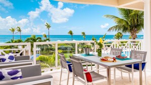A terrace with a table set for dining, overlooking a beach with palm trees and the ocean.