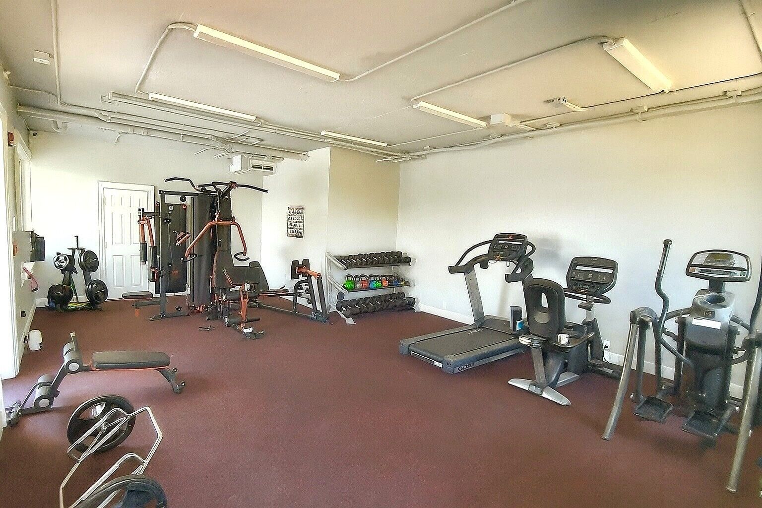 Un gimnasio con diverso equipo de ejercicio, incluyendo cintas de correr, máquinas de pesas y mancuernas.