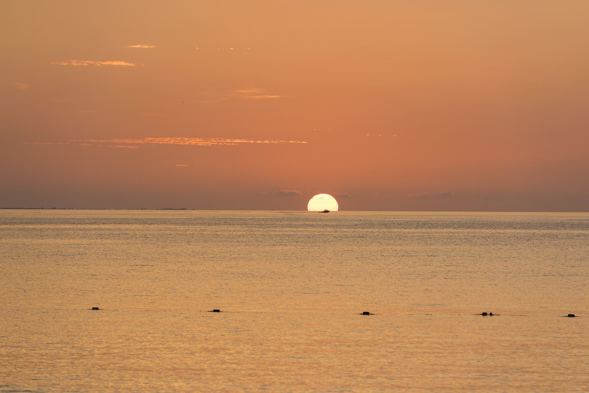 A sunset over a calm sea with a boat in the distance.