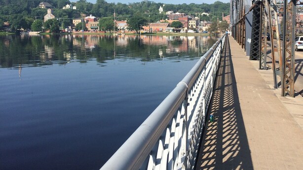 Eine Brücke mit Metallgeländer und ruhigem Wasser darunter.
