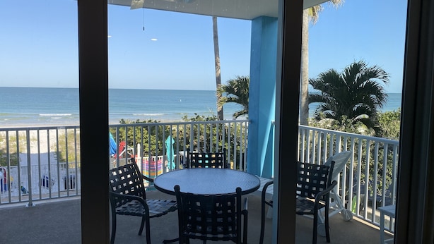 Een balkon met een tafel en stoelen, met uitzicht op een strand en de oceaan.