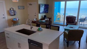Een moderne keuken met een groot eiland, een zithoek met stoelen, en uitzicht op de oceaan door grote ramen.