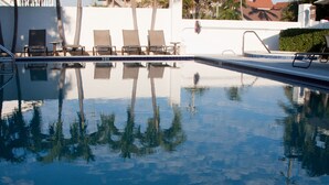 Une piscine aux eaux cristallines dans laquelle se reflètent les palmiers et les chaises longues.