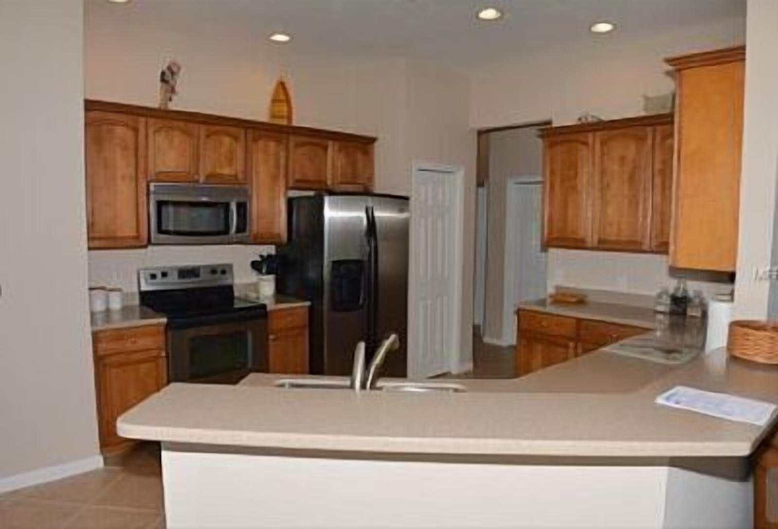 A kitchen with wooden cabinets, a stainless steel refrigerator, a microwave, and a stove.