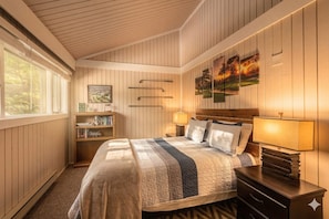 A bedroom with a bed, bedside lamps, a nightstand, a bookshelf, and a painting on the wall. - Views of the Woods - with Pool | Game room | Close to Golf (Bellaire)