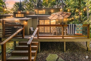 A deck with a wooden staircase, outdoor seating, and string lights. - Views of the Woods - with Pool | Game room | Close to Golf (Bellaire)