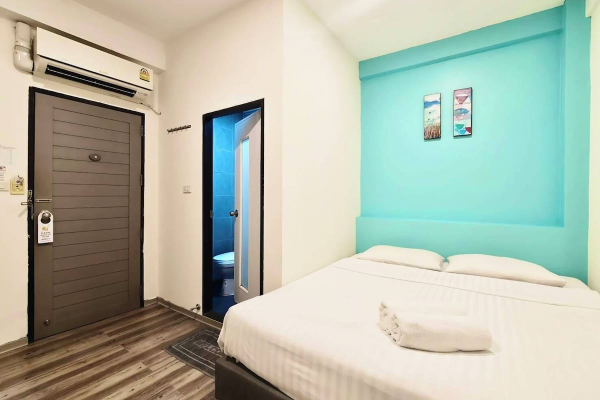 A hotel room with a bed, a bathroom with a toilet, and an air conditioning unit.