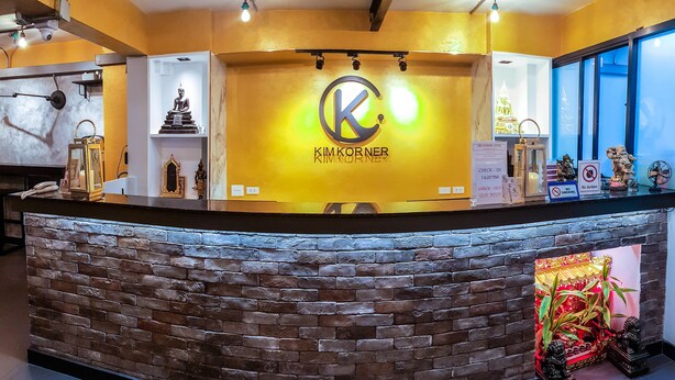 A reception desk with a 'KIMKORNER' sign, a brick wall, and a decorative plant display. - Kim Korner Hotel (Bangkok)