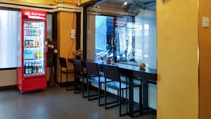 A bar area with a red Coca-Cola refrigerator, black chairs, and a window with a view of the street. - Kim Korner Hotel (Bangkok)