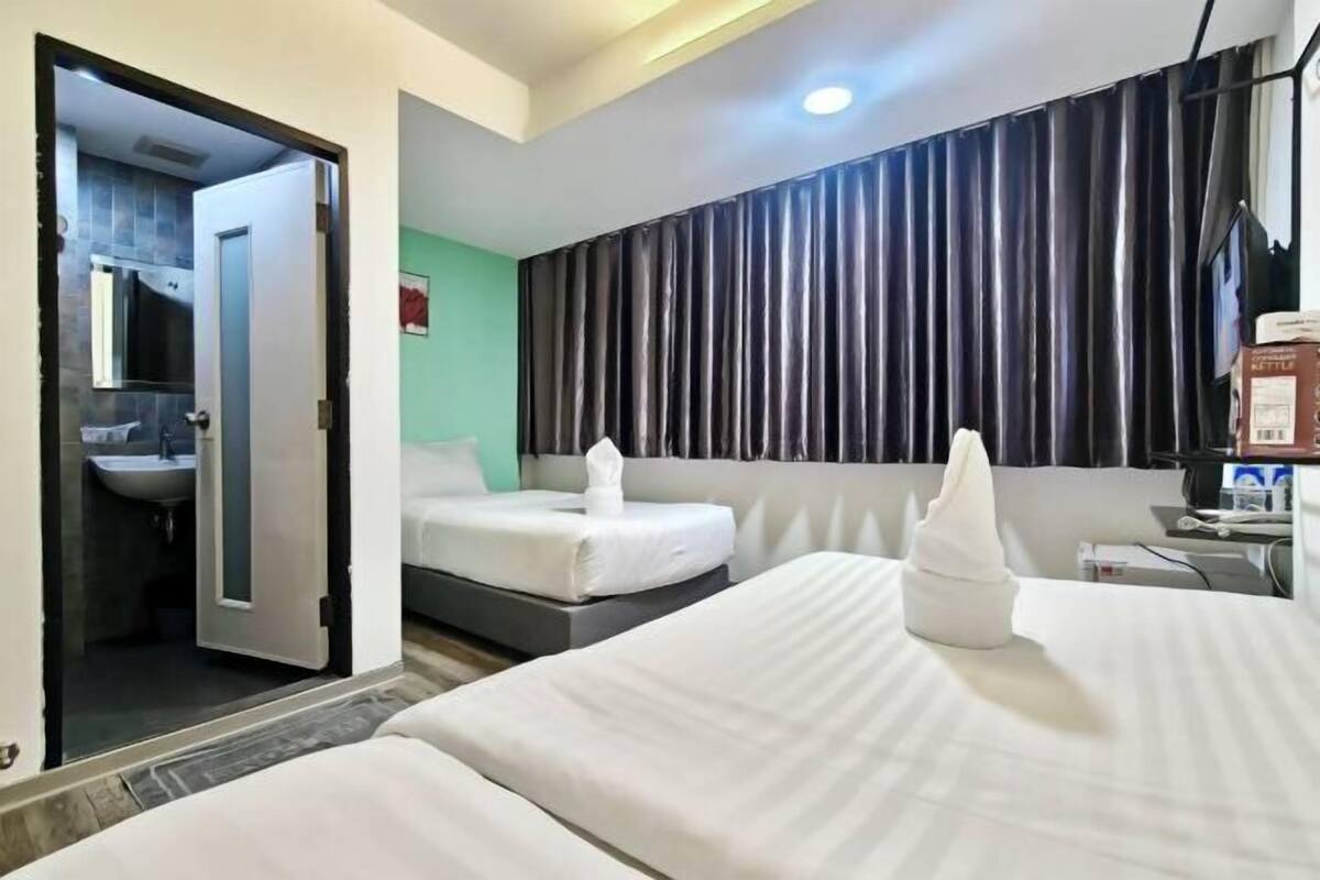 A hotel room with two beds, a bathroom, a desk with a computer, and a large window with curtains.