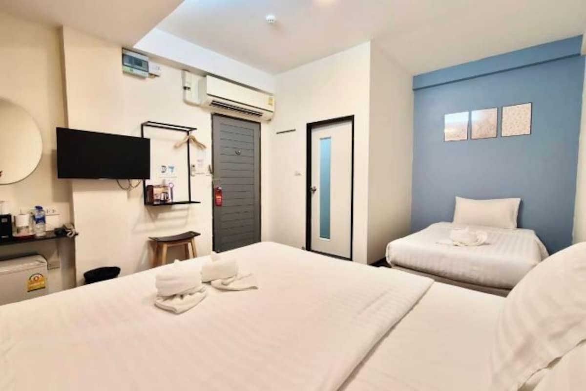 A hotel room with two beds, a TV mounted on the wall, a small table, and a door.