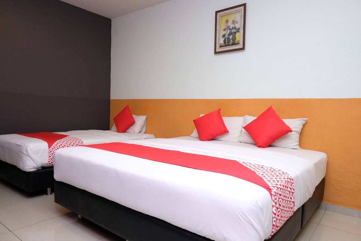 Habitación de hotel con dos camas, cada una con ropa blanca y detalles rojos, un cuadro en la pared y piso de baldosas.