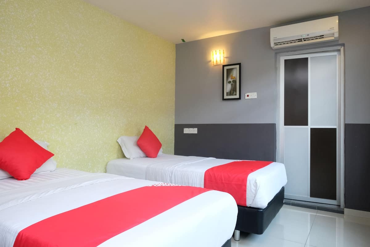 Habitación de hotel con dos camas, cada una con ropa de cama roja y blanca, una pared gris y blanca, un cuadro enmarcado y un equipo de aire acondicionado.