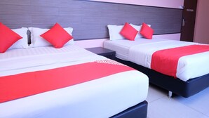 Dos camas de matrimonio con ropa de cama roja y blanca, un cabecero gris y una mesita de noche con una lámpara.