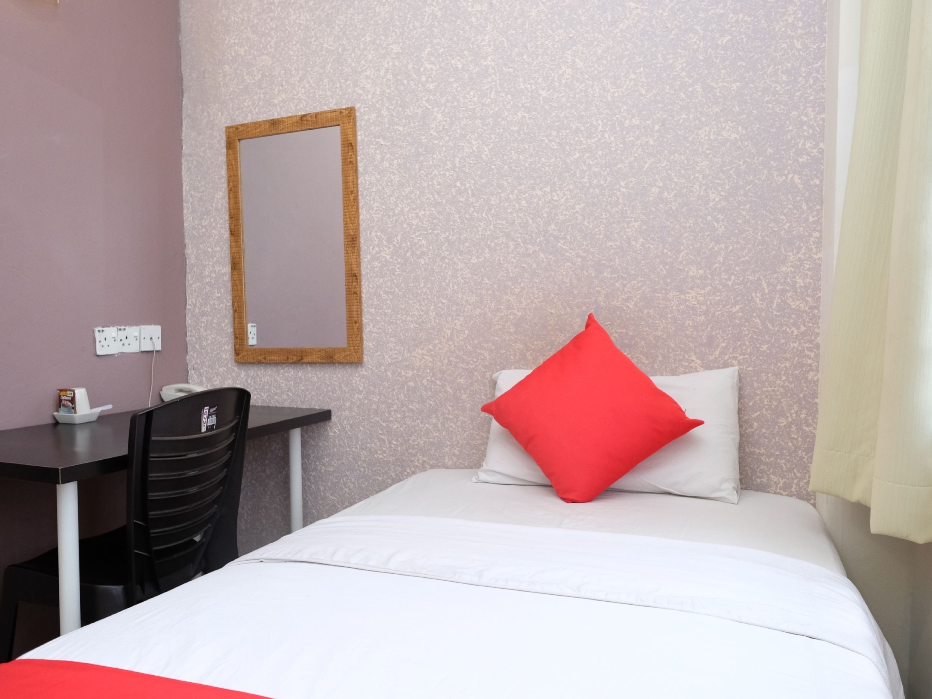Habitación de hotel con cama, escritorio, silla, espejo y enchufe de pared.