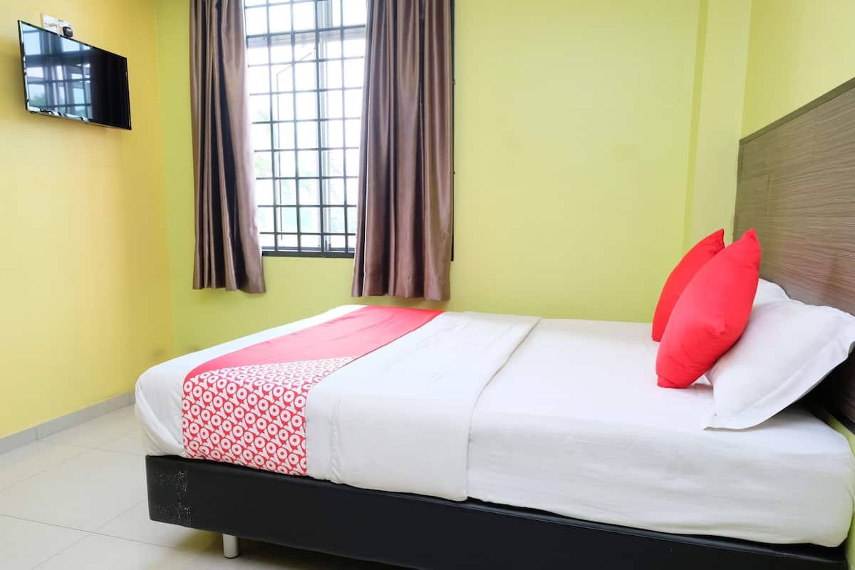 Una cama con una colcha estampada, almohadas rojas y un televisor montado en la pared.