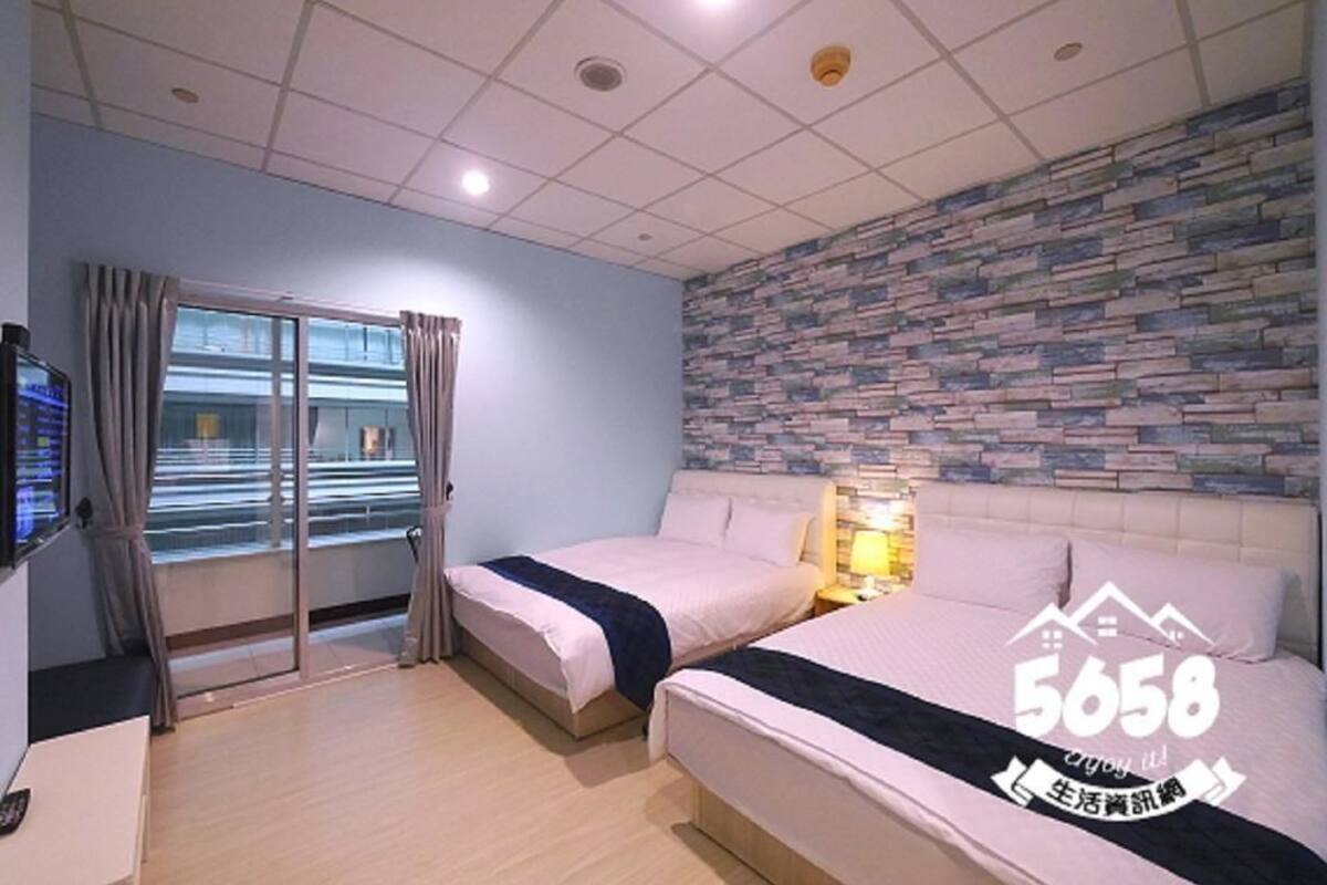 A hotel room with two beds, a stone-patterned wall, a TV, and a sliding glass door to the outside.