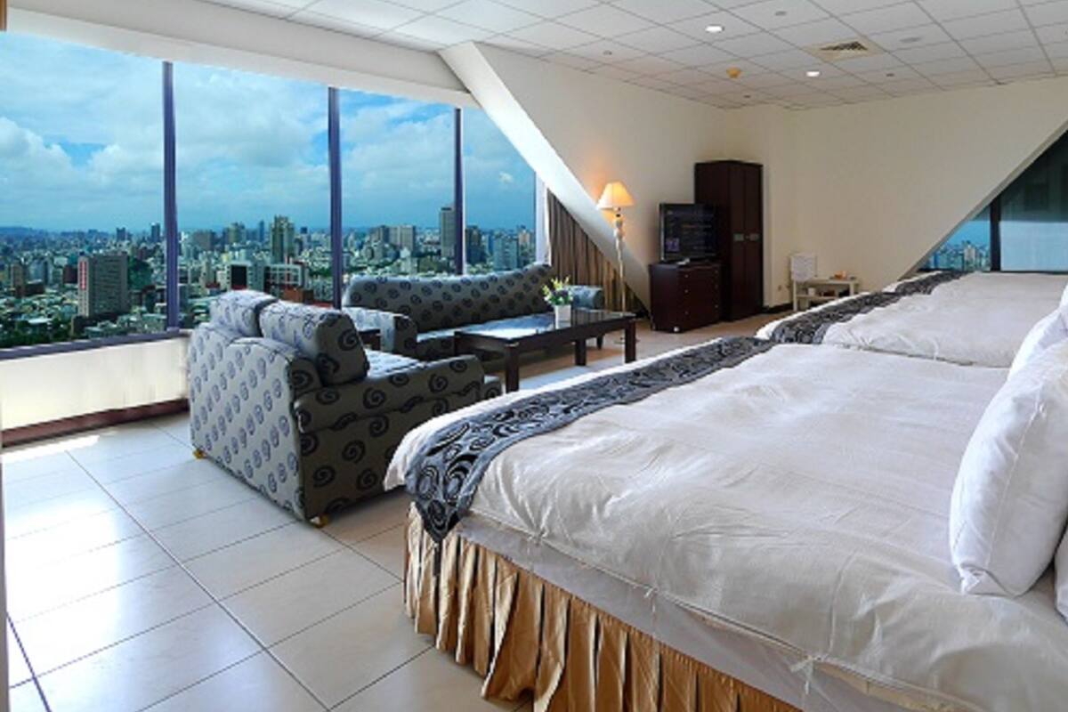 A high-ceiling room with a large bed, a sofa, and a view of a cityscape.