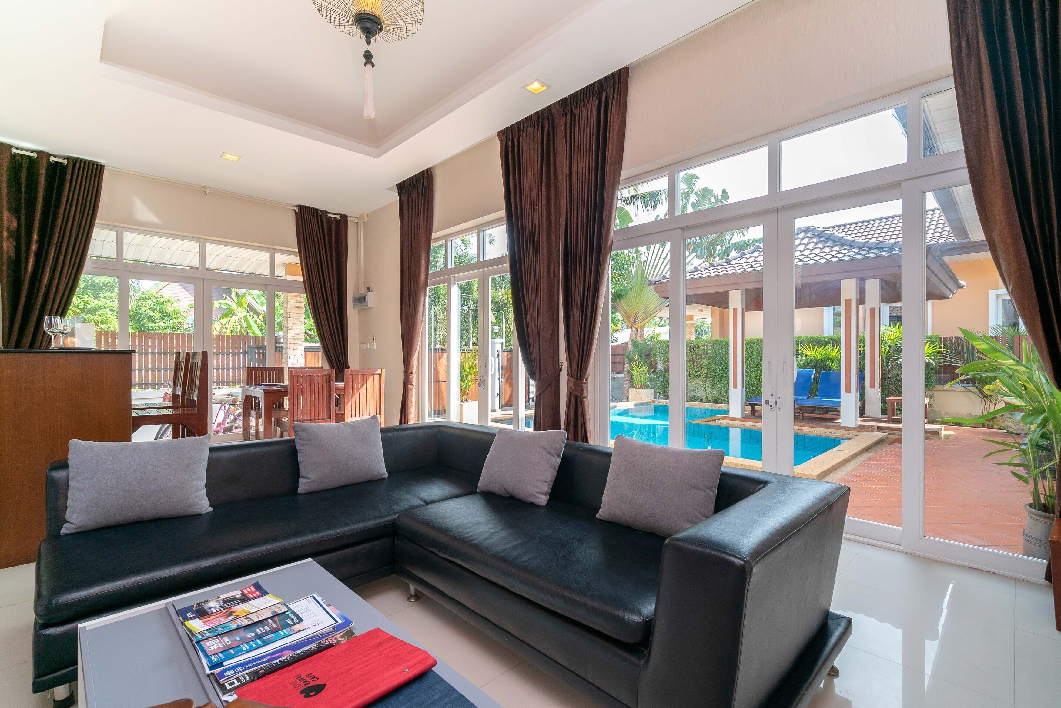 Una sala de estar moderna con un sofá modular, una mesa de centro con revistas y grandes ventanales con vistas a una piscina y zona exterior.