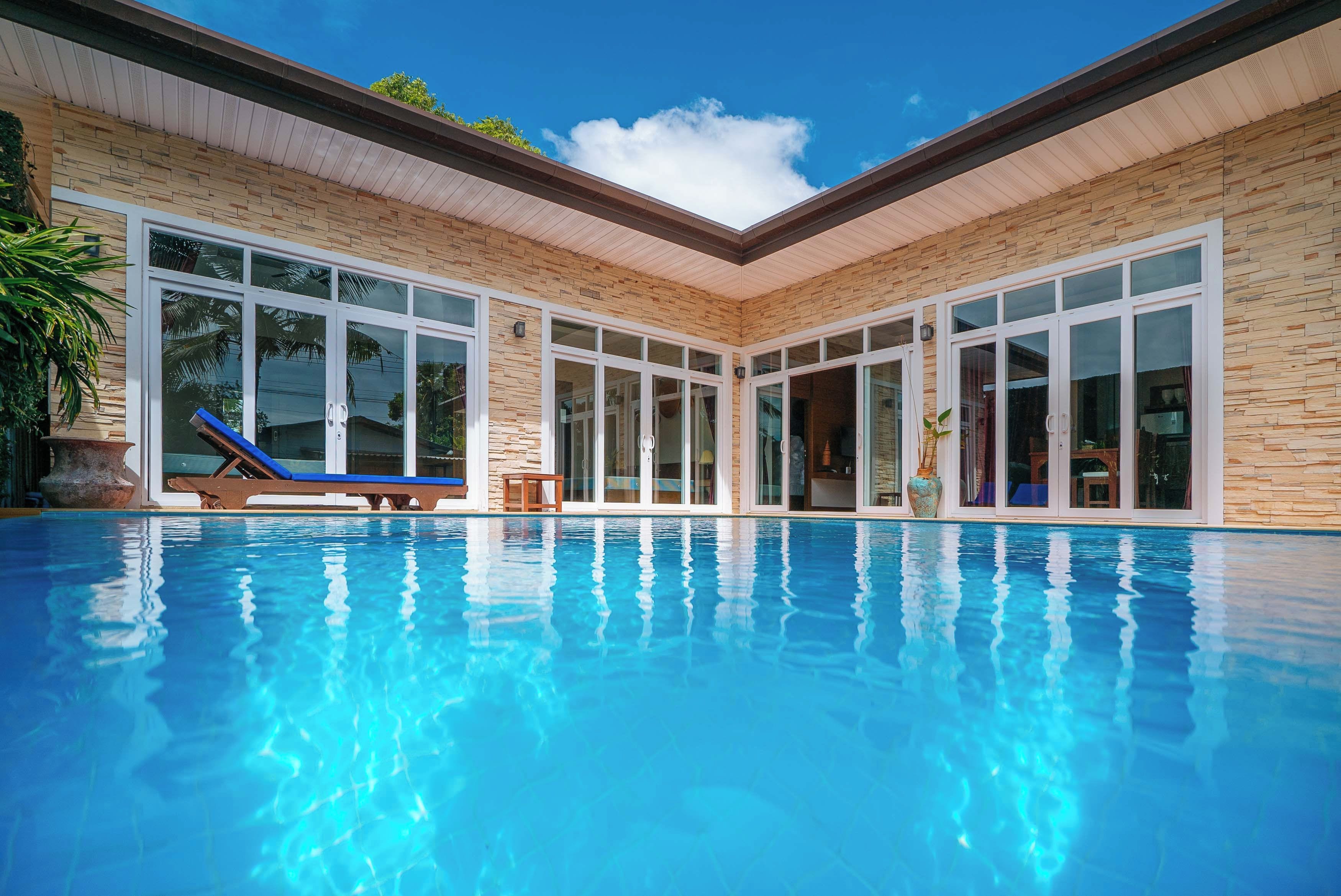 A swimming pool with clear blue water, surrounded by a building with large windows and a stone facade.