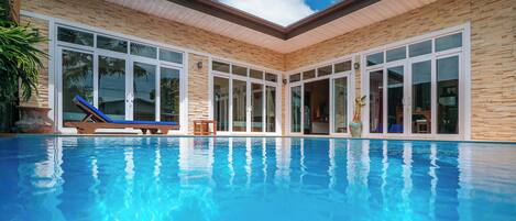 A swimming pool with clear blue water, surrounded by a building with large windows and a stone facade.