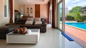 Una sala de estar moderna con un sofá grande, una mesa de centro con adornos y vistas a una piscina a través de amplios ventanales.