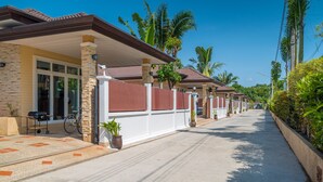 Filas de casas con un corredor techado, palmeras y cielo despejado.