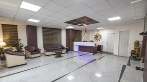 Um hall amplo com balcão de recepção, sofás de couro e uma mesa de centro.